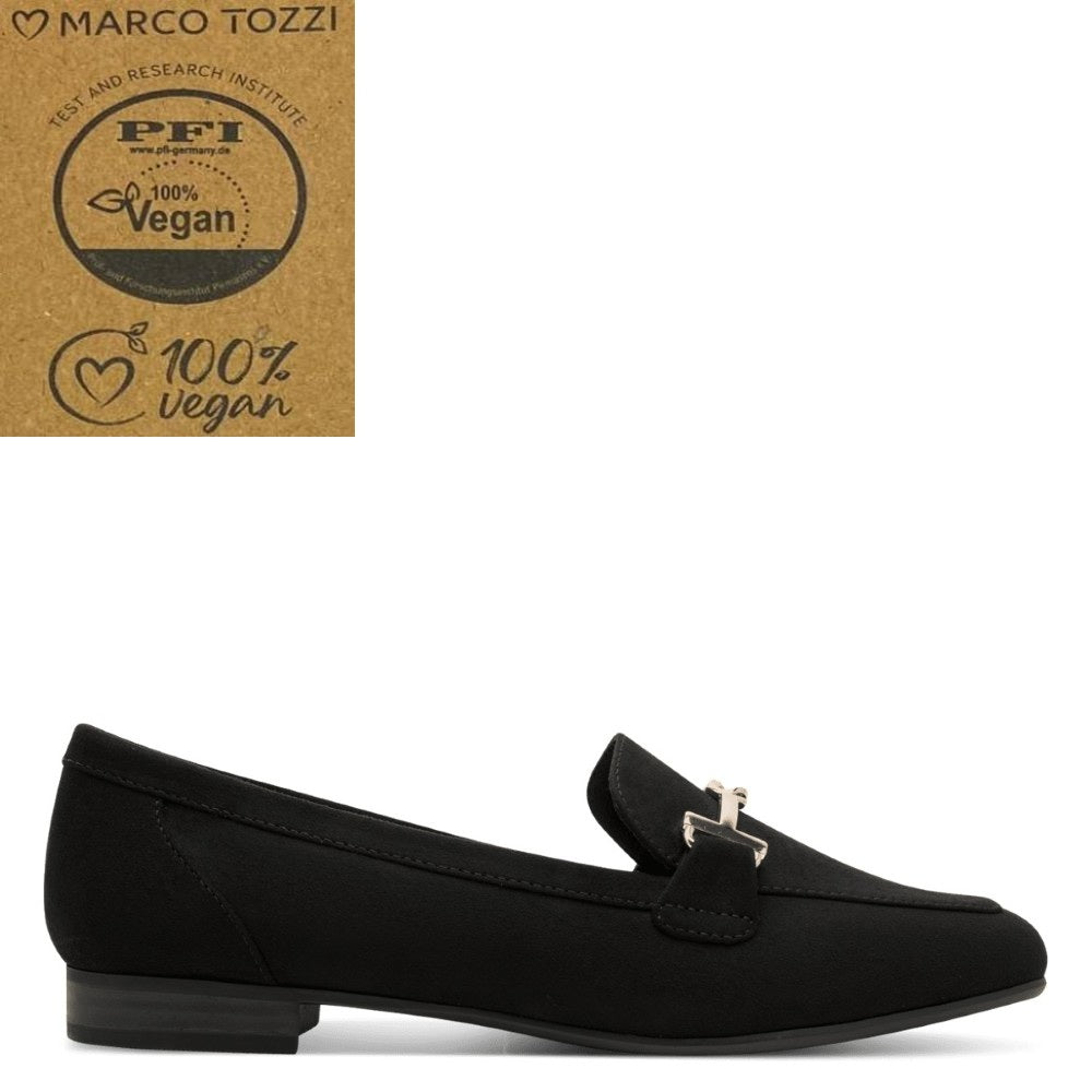 A black suede loafer flat shoe with a small gold-tone metal horsebit detail on the strap, shown in profile against a white background. A brown cardboard certification badge for 'Marco Tozzi 100% Vegan' is shown in the top-left corner.