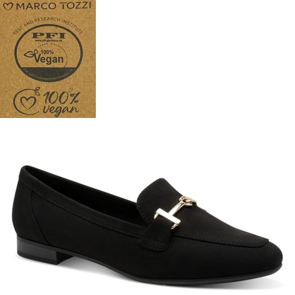 A black suede loafer with a gold-tone metal 'H' accent on the vamp, shown from a side profile against a white background. In the top-left corner, there is a brown cardboard badge featuring the Marco Tozzi brand logo and a '100% Vegan' certification seal.