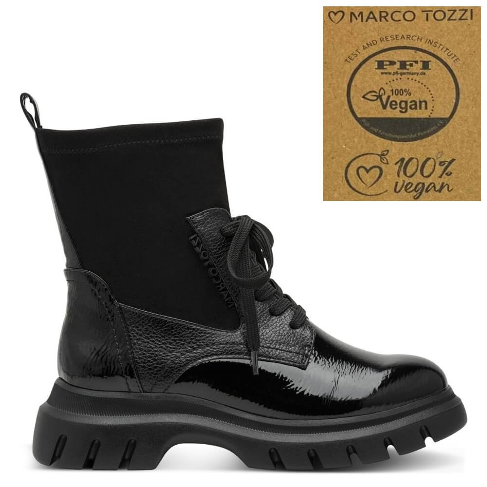 A Marco Tozzi  black ankle boot with a glossy patent leather toe and heel, a textured leather midfoot, a black elastic side panel, and a chunky lug sole. An inset badge in the top right displays a '100% Vegan' certification logo from PFI  