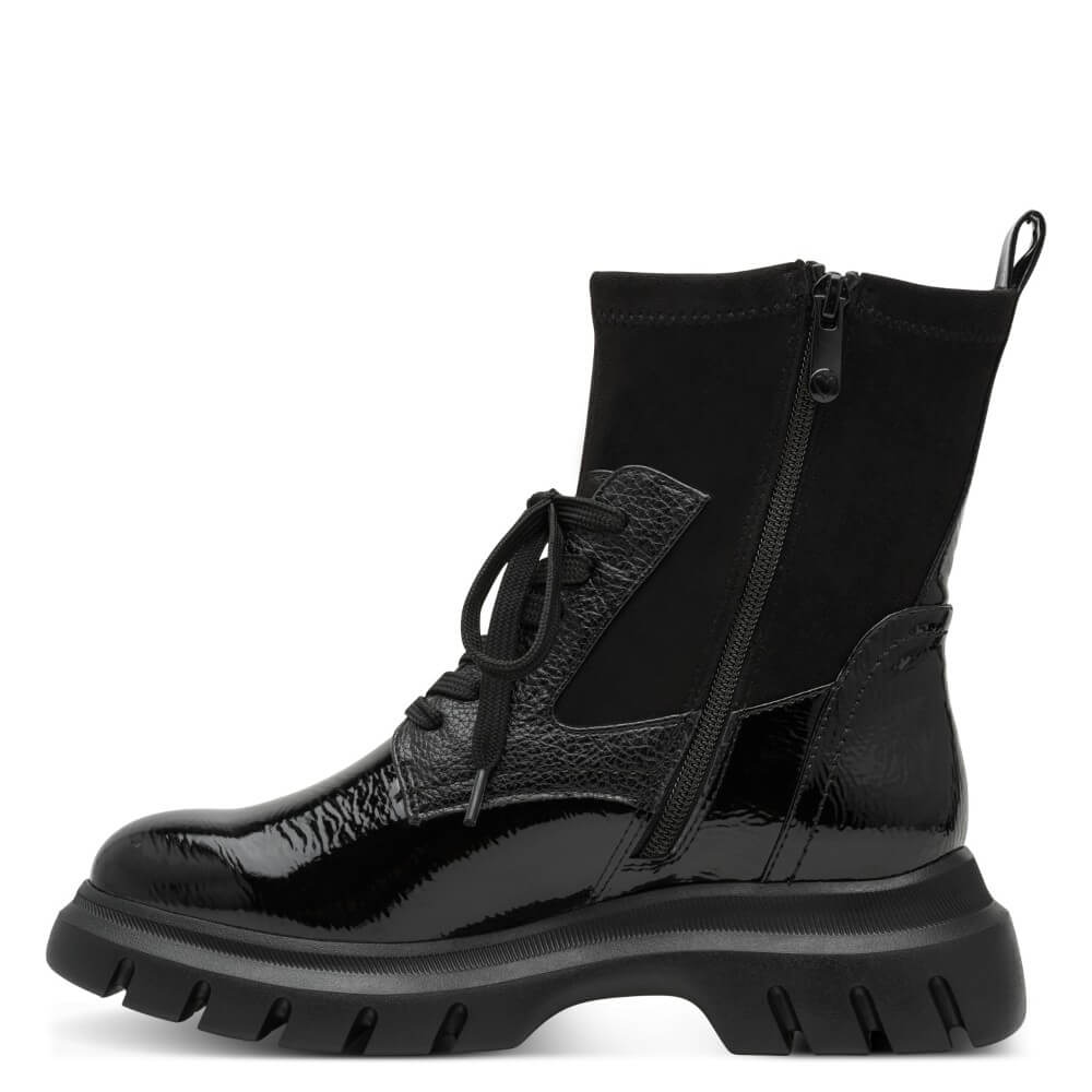 A Marco Tozzi Vegan black ankle boot with a glossy patent leather toe, textured side panel, black laces, a side zipper, and a chunky lug sole, shown against a plain white background.