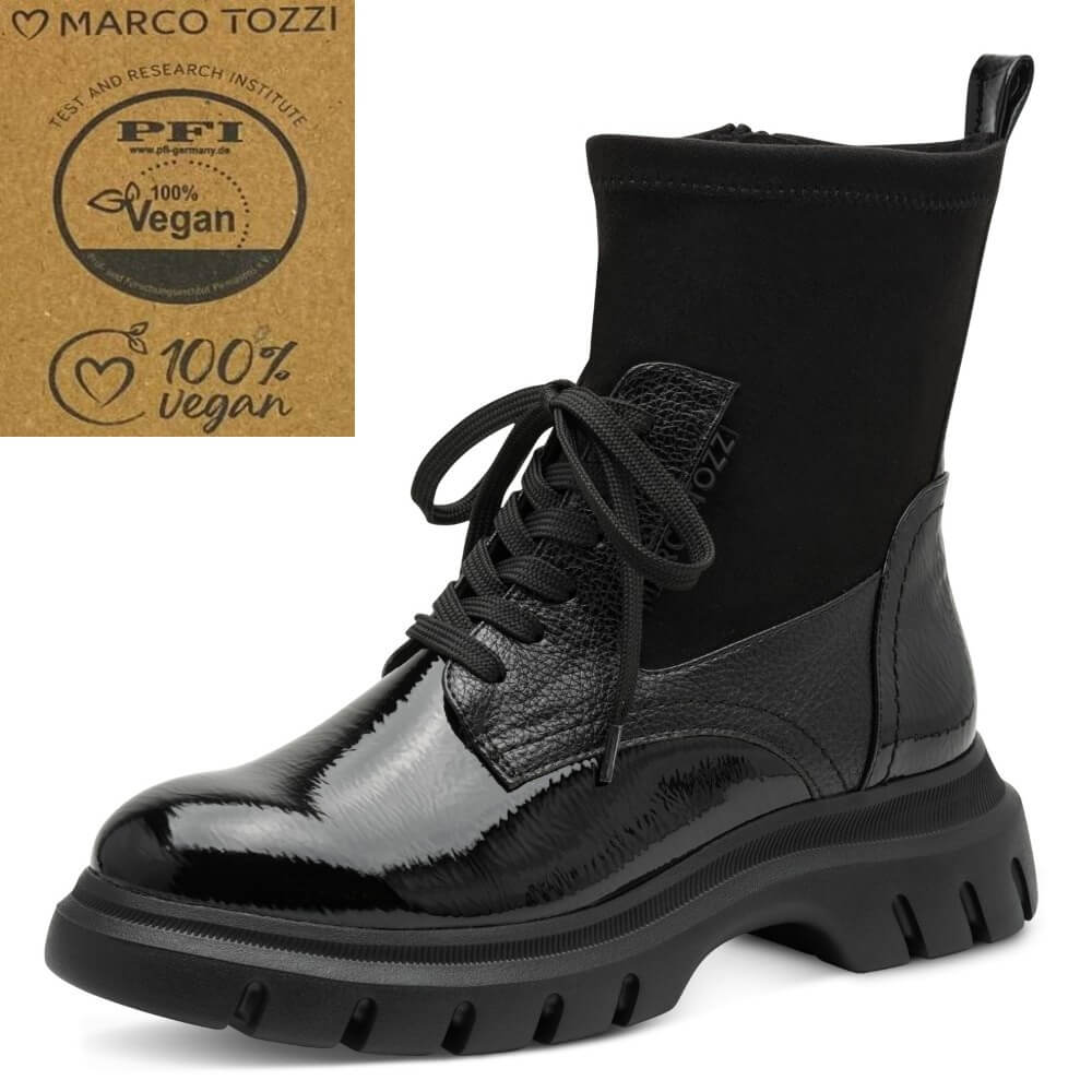 A Marco Tozzi  black ankle boot with a glossy patent leather toe and heel, a textured leather midfoot, a black elastic side panel, and a chunky lug sole. An inset badge in the top right displays a '100% Vegan' certification logo from PFI  