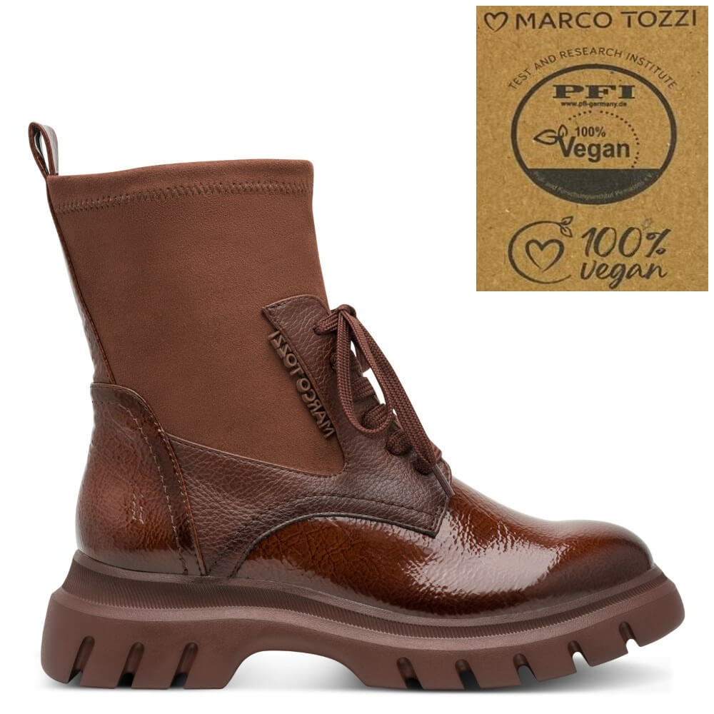 A Marco Tozzi brown ankle boot with a glossy patent leather toe and side panel, a suede-like upper, and a chunky lug sole, shown on a white background with a Marco Tozzi vegan certification badge in the top right corner.