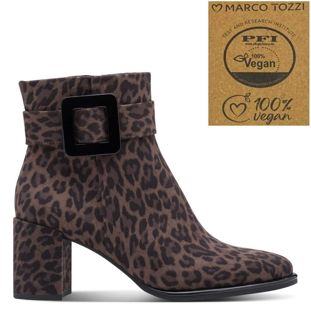 A Marco Tozzi brown and black leopard print ankle boot with a chunky block heel and a wide strap across the ankle featuring a large black square buckle. An inset in the top right shows a certification badge for 'Marco Tozzi' and 'PFI 100% Vegan'.