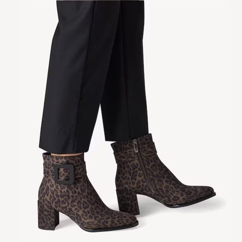 A pair of Marco Tozzi women's ankle boots with a brown and black leopard print, styled with black trousers. The boots feature a block heel, a side zipper, and a decorative buckle on the outer ankle strap.