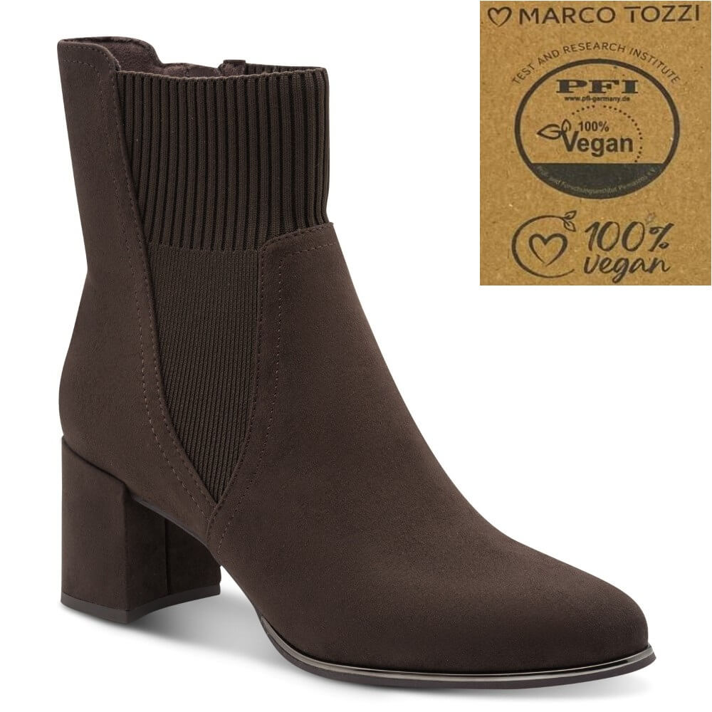 A dark brown suede ankle boot with a ribbed elastic side panel and a block heel, shown on a white background with a 'Marco Tozzi' vegan certification badge in the top right corner.