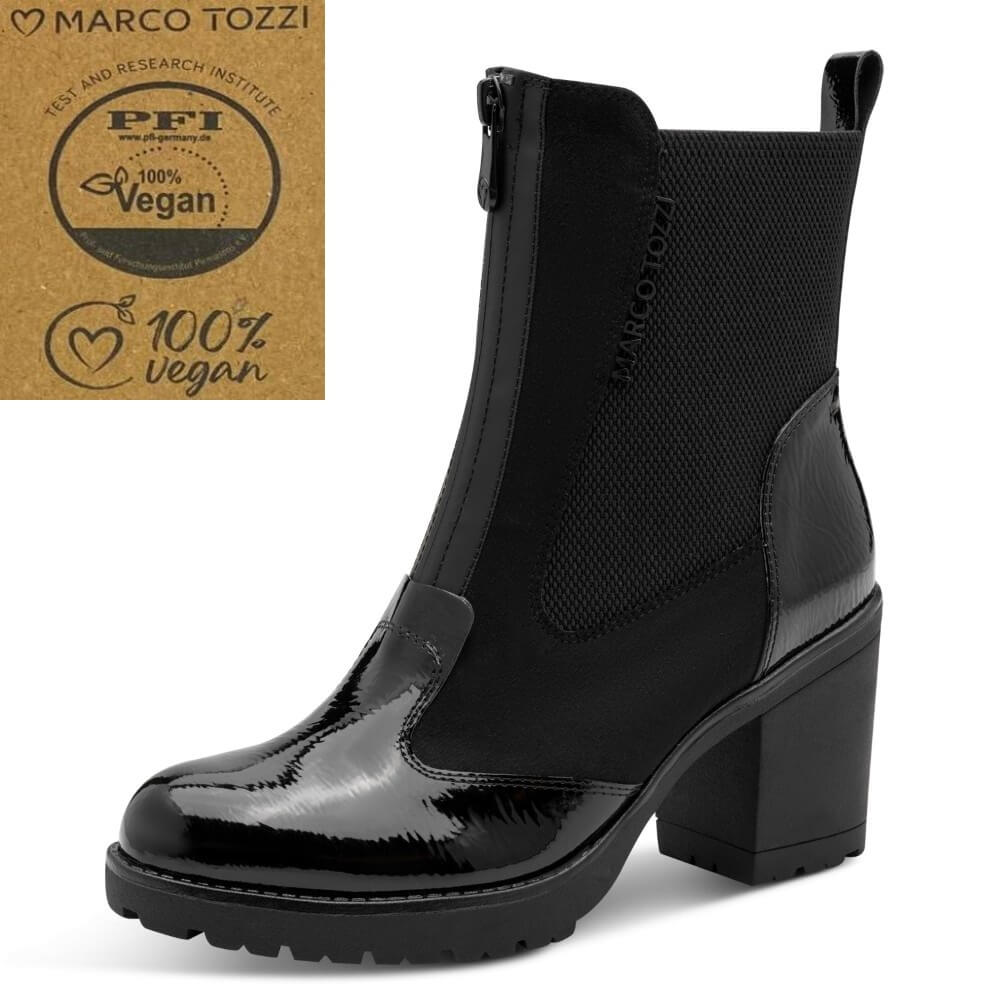 A black ankle boot with a glossy patent leather toe, elastic side panels, and a chunky block heel, shown on a white background. A kraft paper badge in the top-left corner reads 'Marco Tozzi' and '100% vegan' with a PFI test logo.