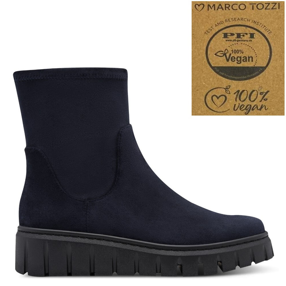 A dark navy blue ankle boot with a thick black lug sole, shown in profile on a white background. In the top right corner, there is a square graphic badge featuring the brand 'Marco Tozzi' and a '100% Vegan' certification logo.