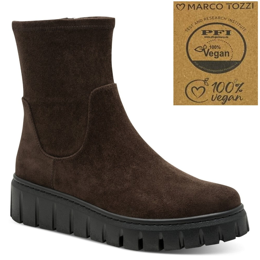 A dark brown suede ankle boot with a chunky black lug sole, shown on a white background with a 'Marco Tozzi 100% Vegan' certification badge in the top right corner.