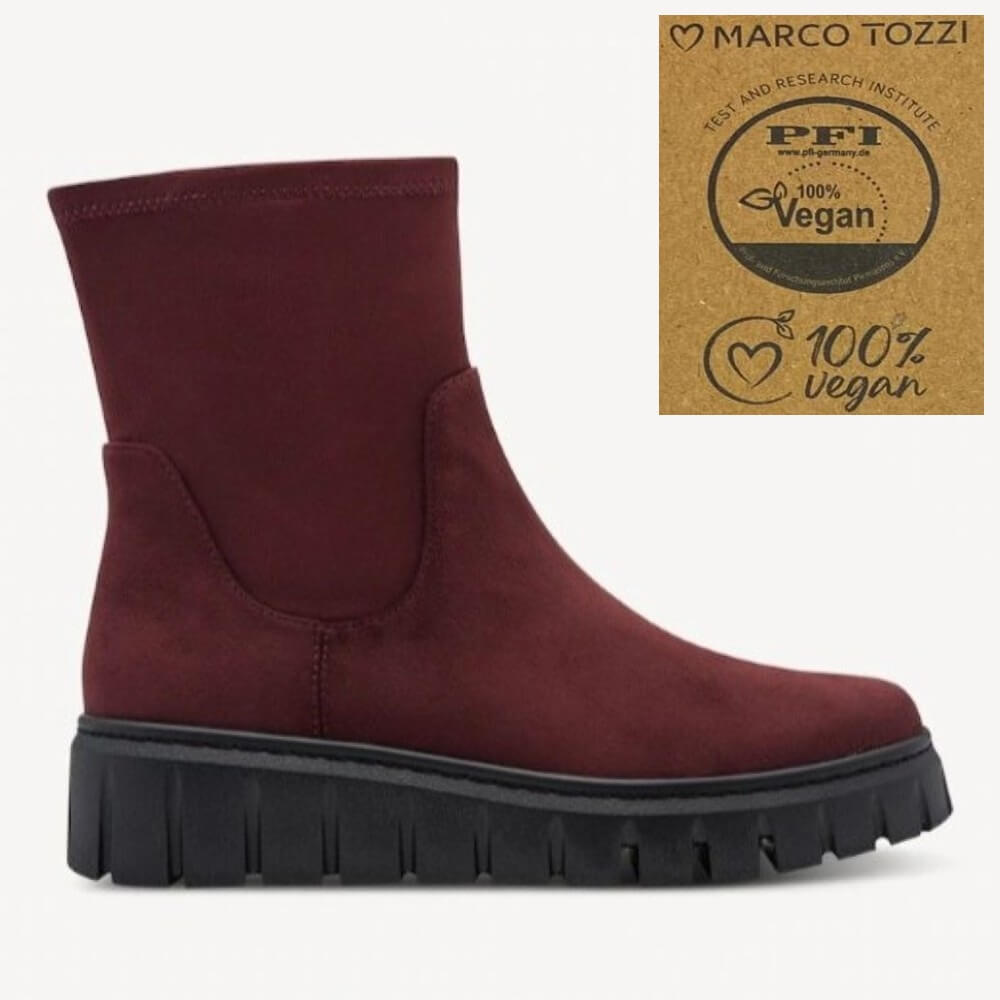 A Marco Tozzi low-top suede ankle boot in burgundy with a chunky black lug sole, shown on a light grey background. An inset badge in the top right reads Marco Tozzi PFI 100% Vegan.