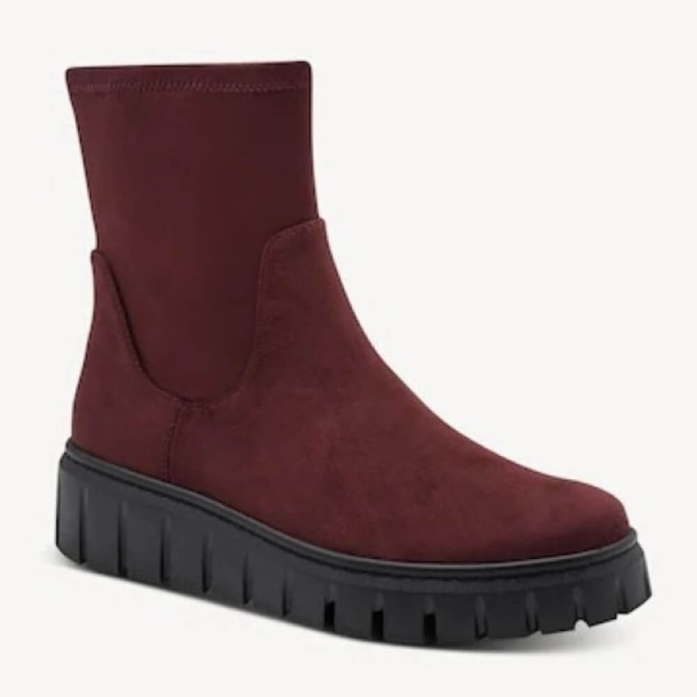 A Marco Tozzi burgundy suede ankle boot with a chunky black lug sole, shown from a three-quarters angle on a light grey background.