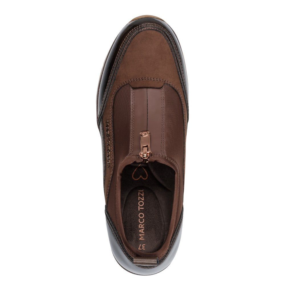 A brown slip-on sneaker by Marco Tozzi, featuring a textured faux-leather upper, a front zipper, and a thick cream-colored platform sole. A certification badge for '100% Vegan' is shown in the top right corner against a white background.