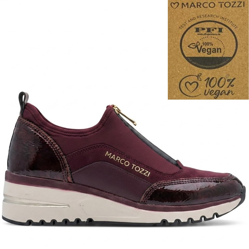 A low-top slip-on sneaker by Marco Tozzi in burgundy and black, featuring a white midsole and a gold zipper. An inset badge on the top right displays a '100% Vegan' certification logo.