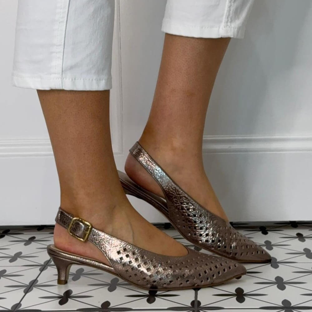  Marian Metallic Bronze Kitten-heeled shoes worn with white pants on a patterned floor.