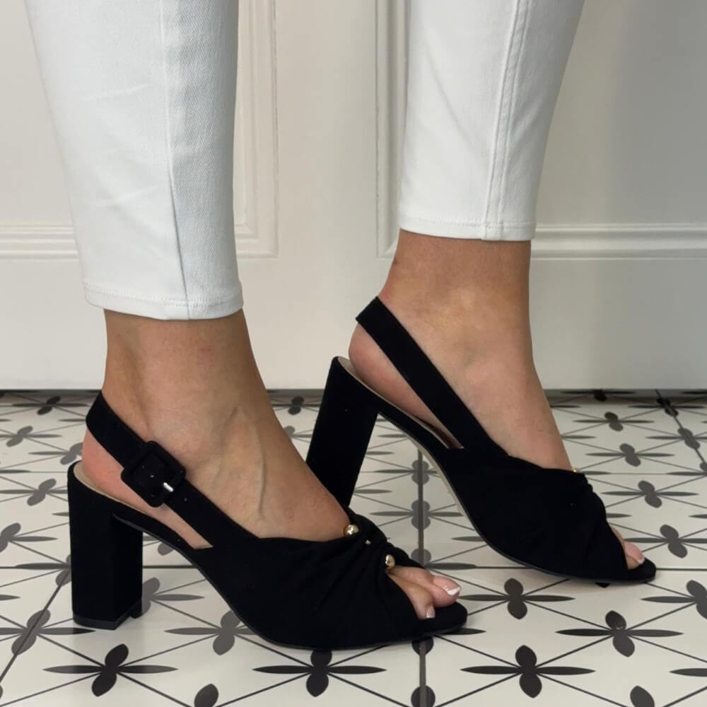 Marian Black open-toe heels worn with white pants on a patterned floor.