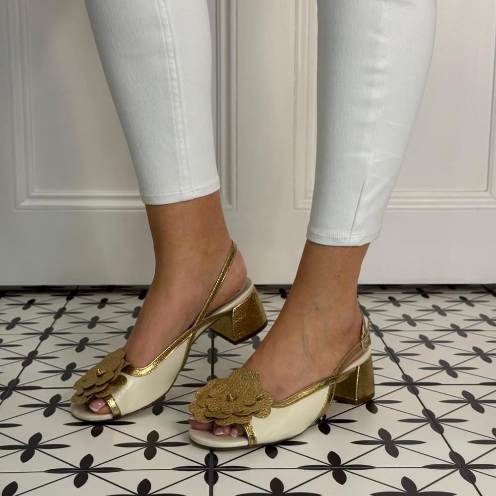 Marian White sandals with gold accents worn by a person on a patterned floor.