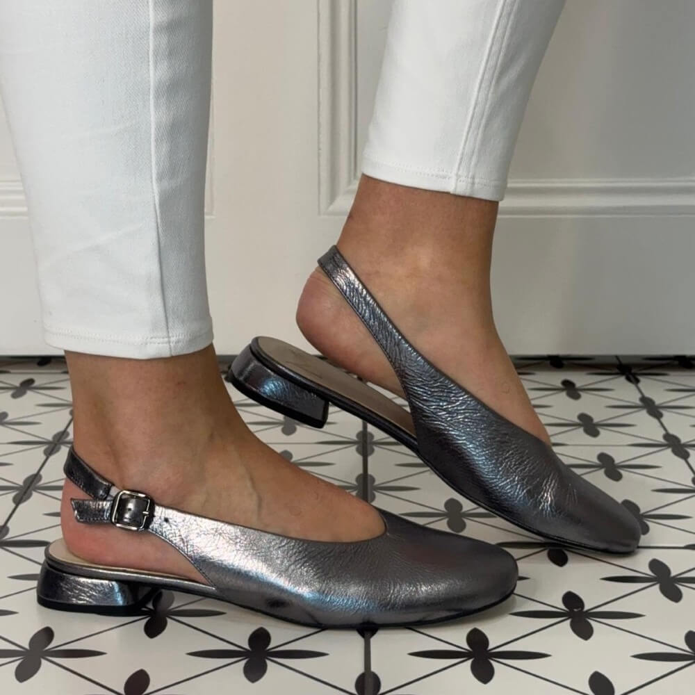 Marian Silver slingback flats worn with white pants on a patterned floor.