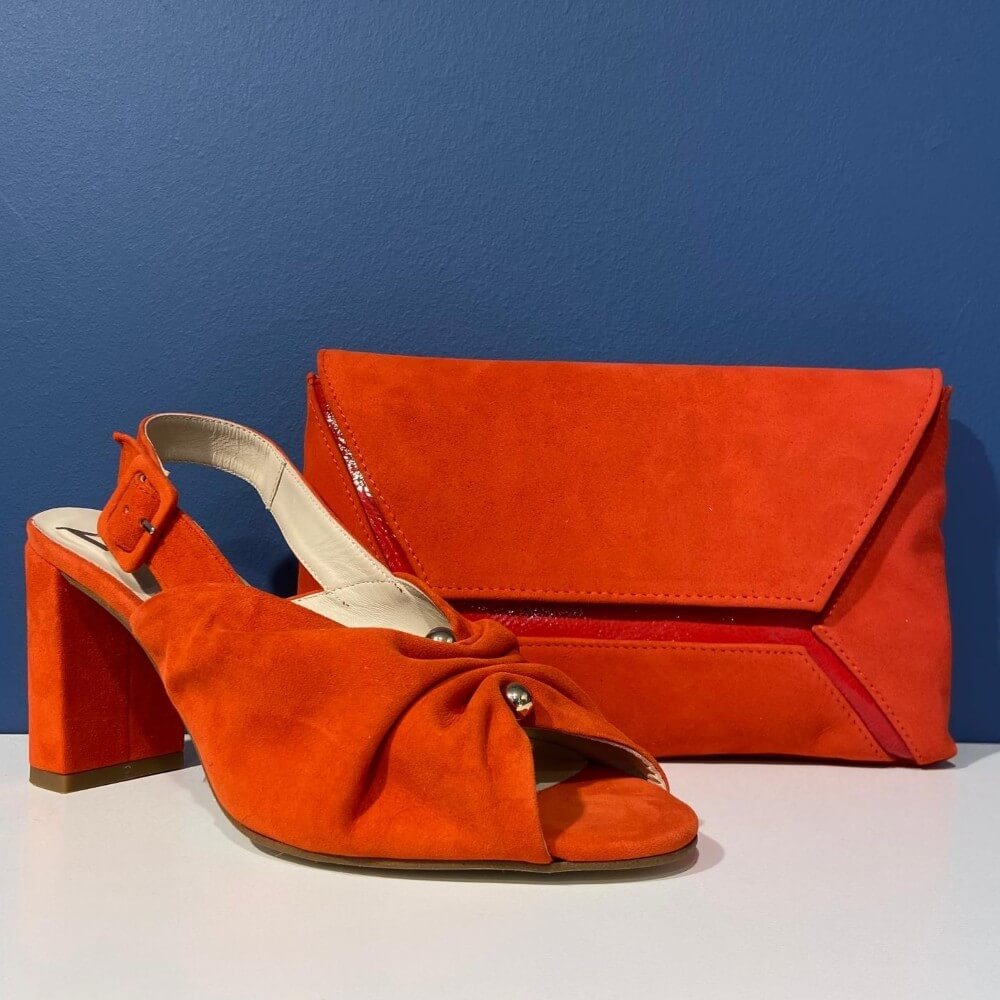 Marian Orange high-heeled shoes with a matching clutch bag on a white surface against a blue background