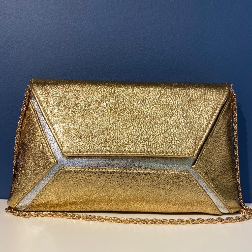 Marian Gold and silver clutch bag with a gold chain on a blue background
