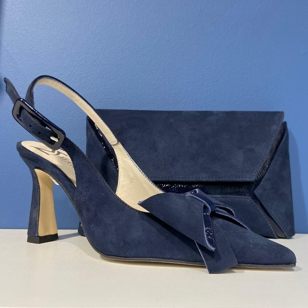 Marian Navy blue high-heeled shoes with a bow and matching clutch against a blue background