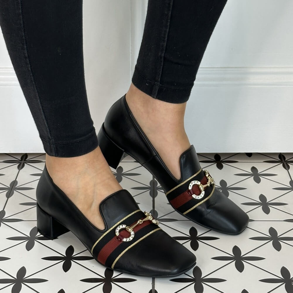 Black leather loafers with red and gold accents worn by a person on a patterned floor.