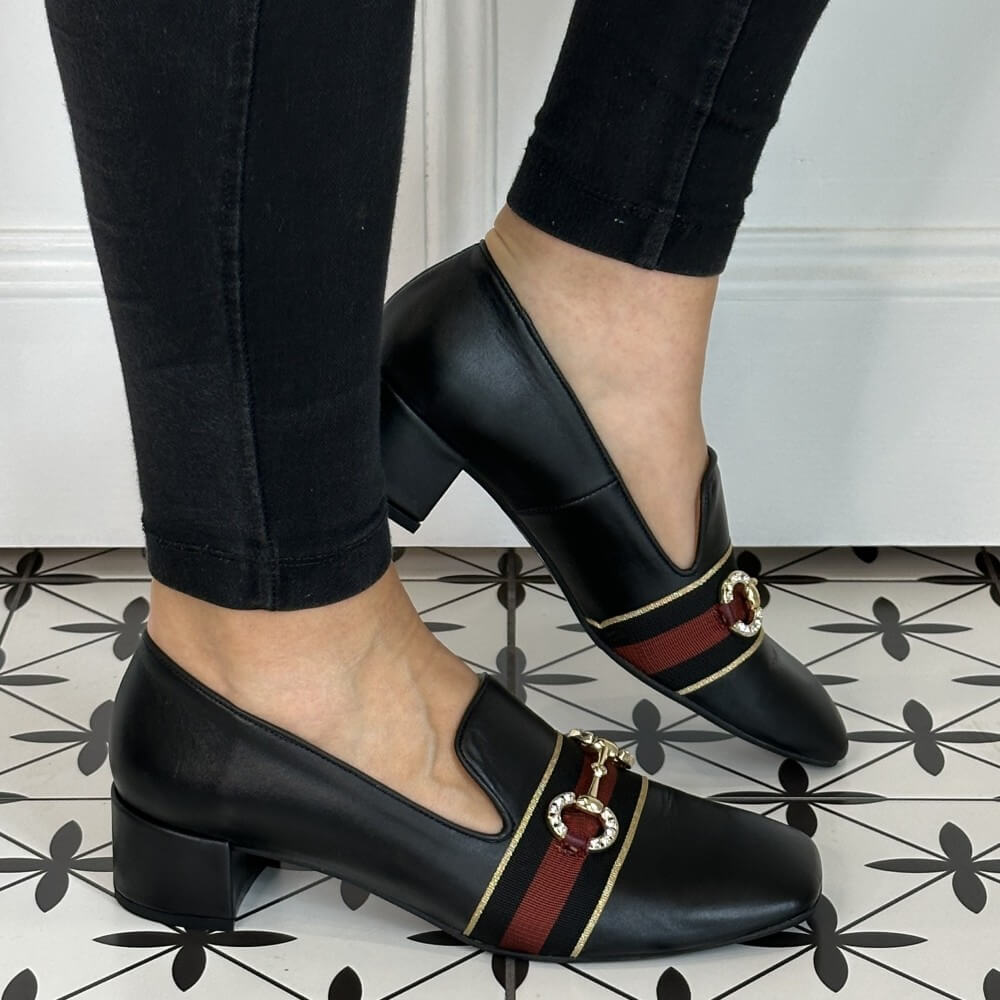 Black leather loafers with red and gold accents worn by a person on a patterned floor.