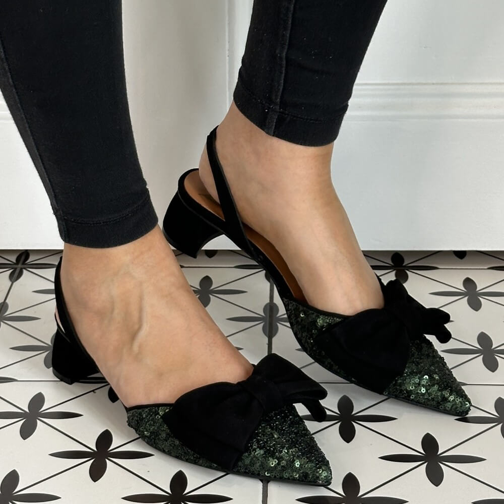 Black pointed-toe shoes with green sequin details worn by a person on a patterned floor.