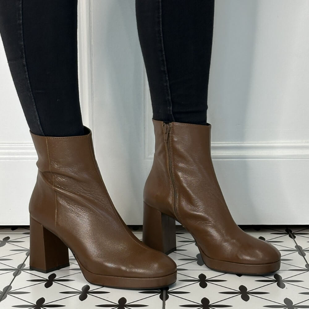 Brown leather platform ankle boots worn with black pants on a patterned floor.