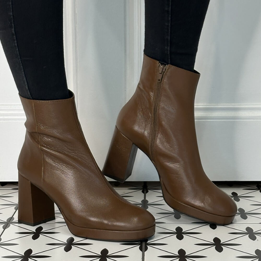 Brown leather platform ankle boots worn with black pants on a patterned floor.