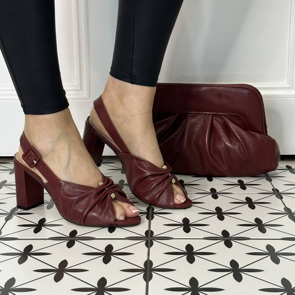 Burgundy leather sandals worn with black leggings on a patterned floor. 