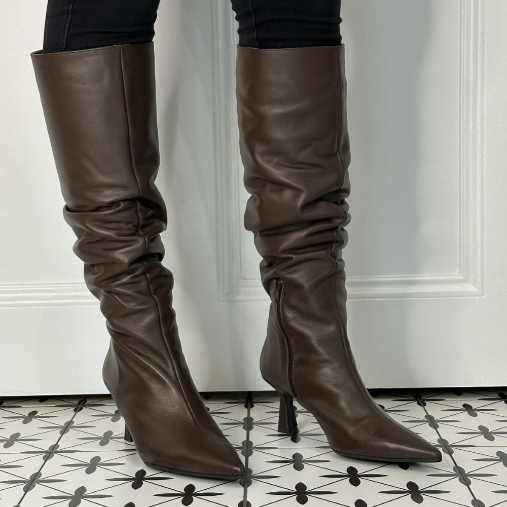 Brown leather knee-high boots with a high heel on a patterned floor.