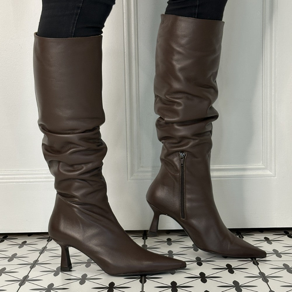 Brown leather knee-high boots with a high heel on a patterned floor.
