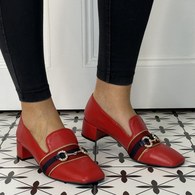 Red leather loafers with black and gold accents worn by a person on a patterned floor.