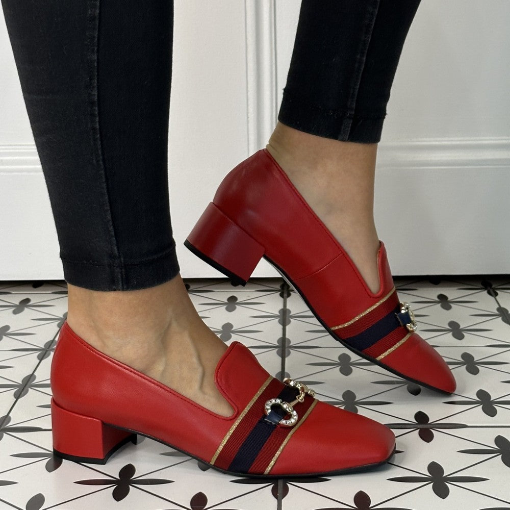 Red leather loafers with black and gold accents worn by a person on a patterned floor.