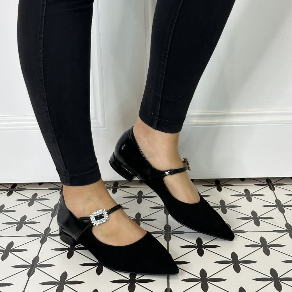 Black Maryjane shoes with decorative buckles worn on a patterned floor.