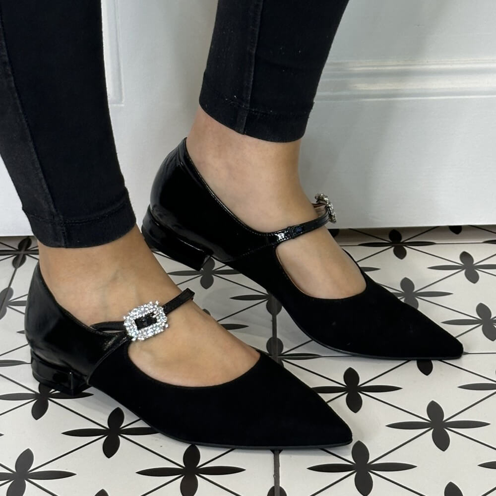 Black Maryjane shoes with decorative buckles worn on a patterned floor.