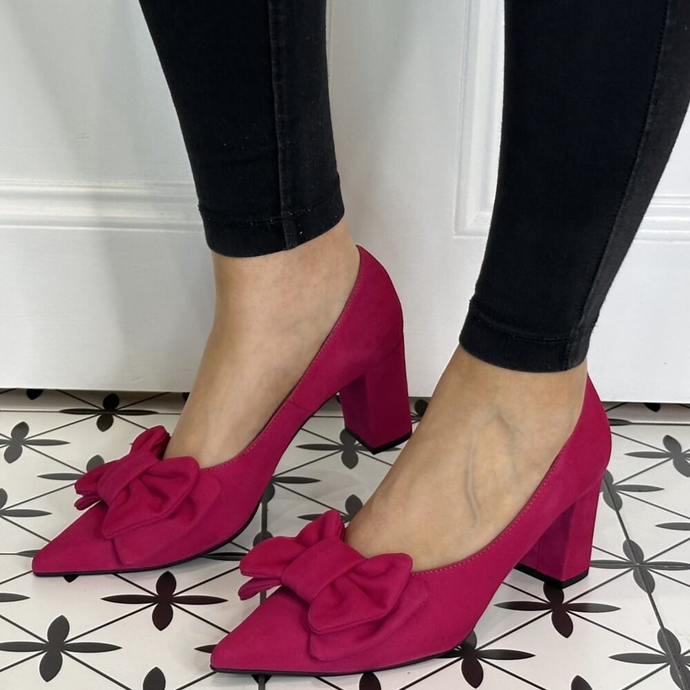 Pink high-heeled shoes with bows worn by a person on a patterned floor.