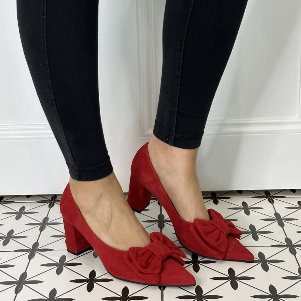 Red high-heeled shoes with bows worn by a person on a patterned floor.