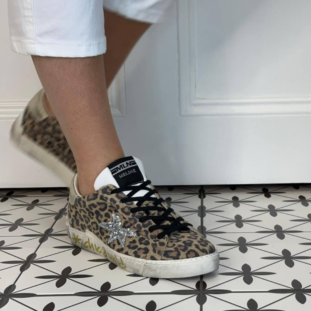 Meline Leopard print sneakers with a star detail worn by a person on a patterned floor.