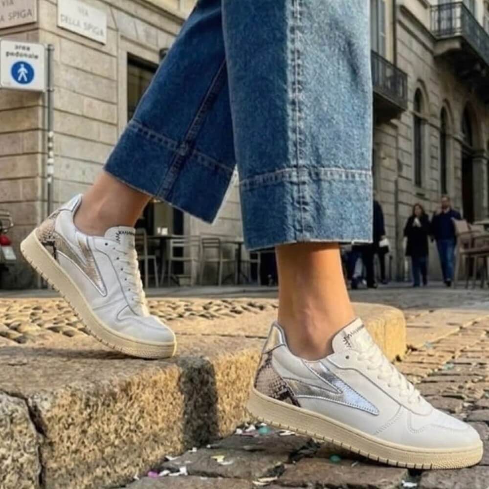 Meline White sneakers with beige soles worn by a person on stone steps in an urban setting.