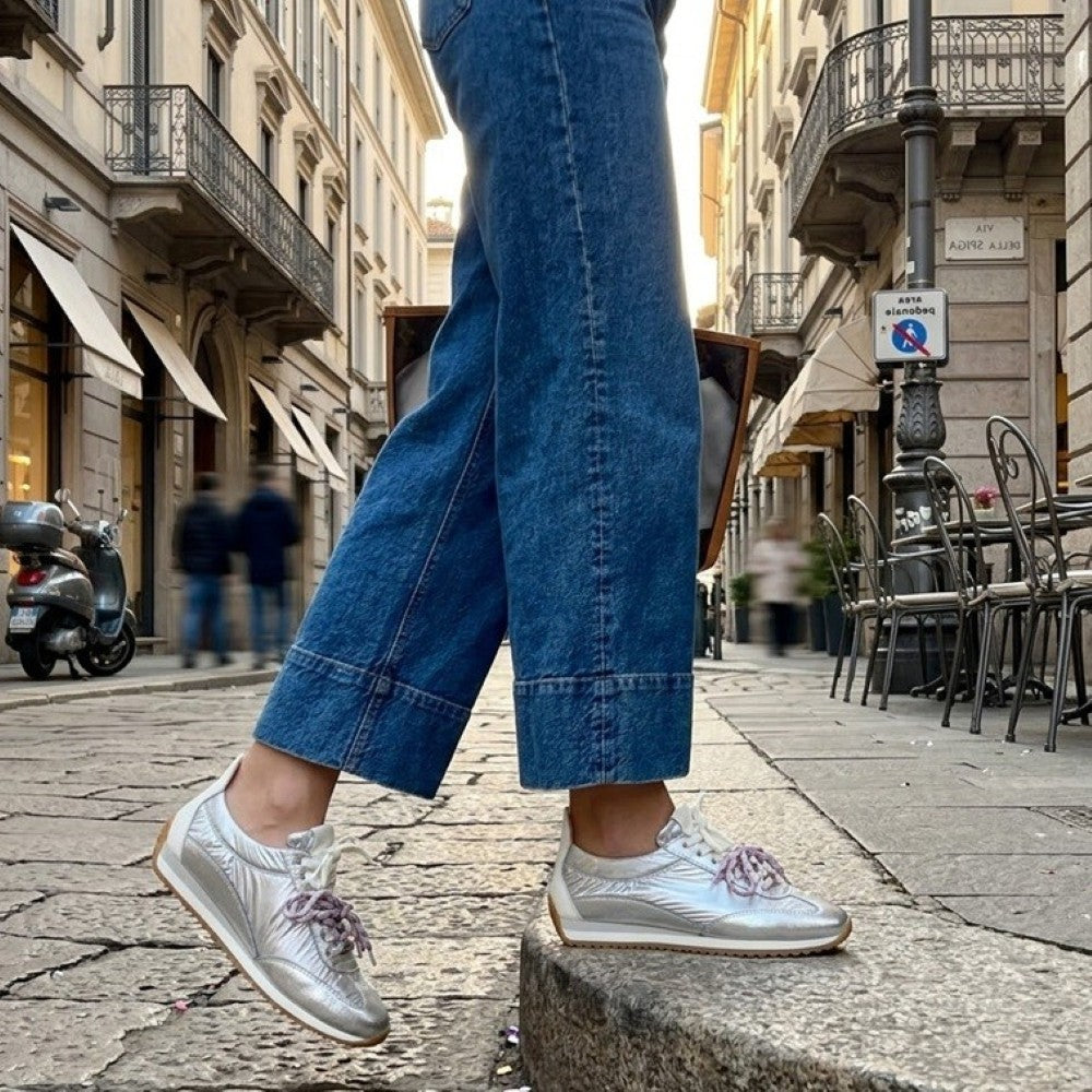 Person wearing Meline silver sneakers with pink laces and blue jeans on a city street.
