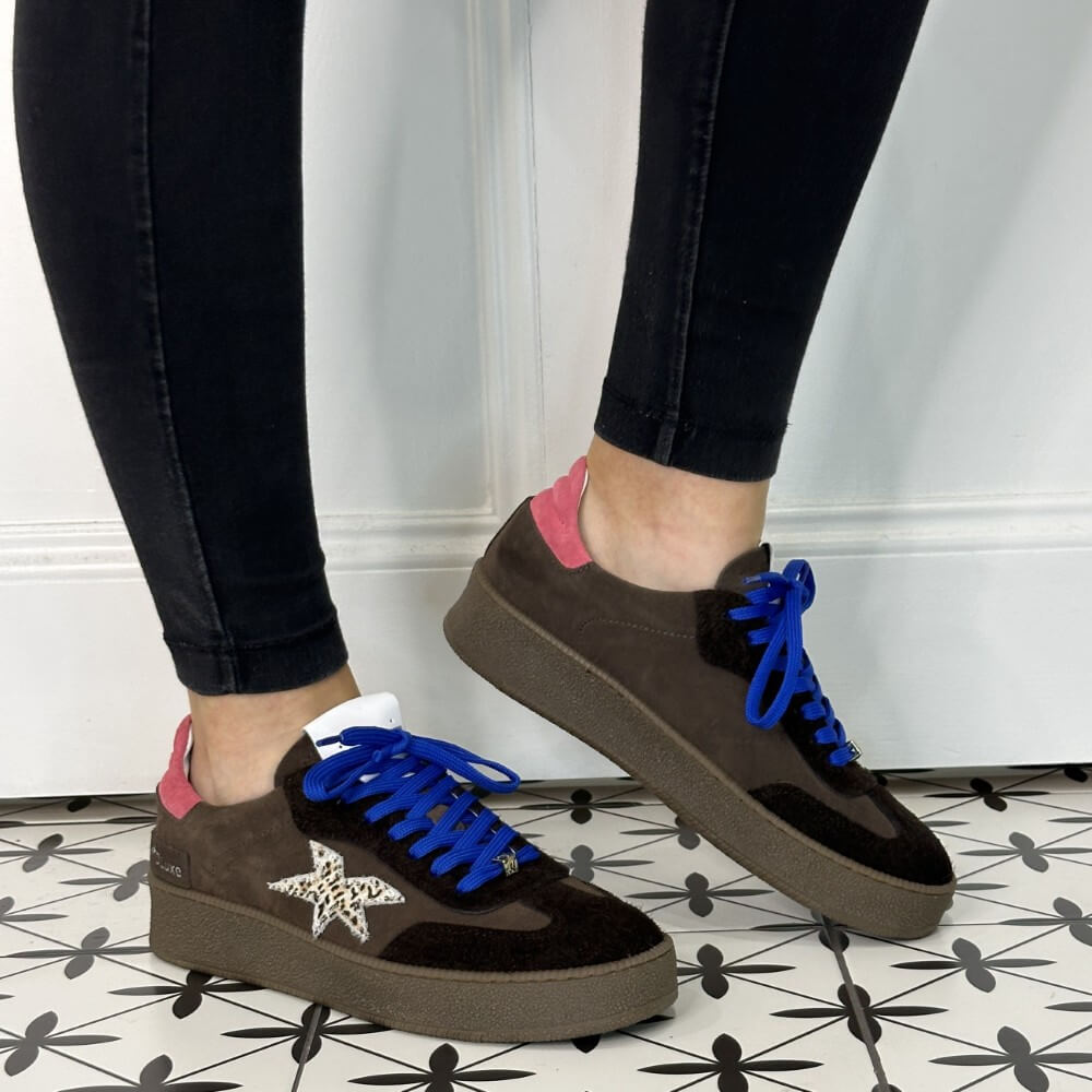 Brown sneakers with blue laces and a pink tab worn with black jeans 