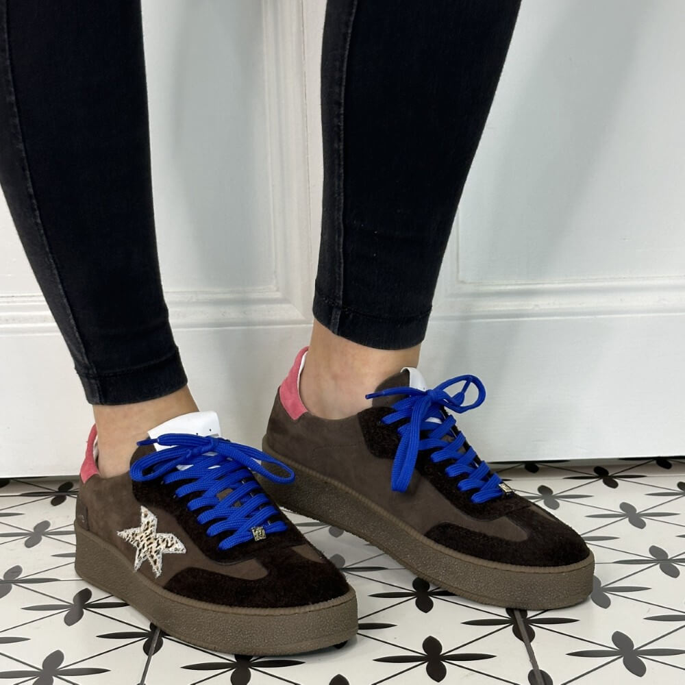 Brown sneakers with blue laces and a pink tab worn with black jeans 