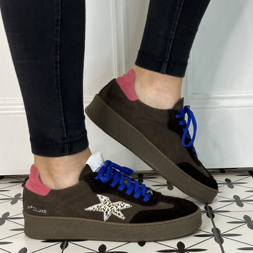 Brown sneakers with blue laces and a pink tab worn with black jeans 