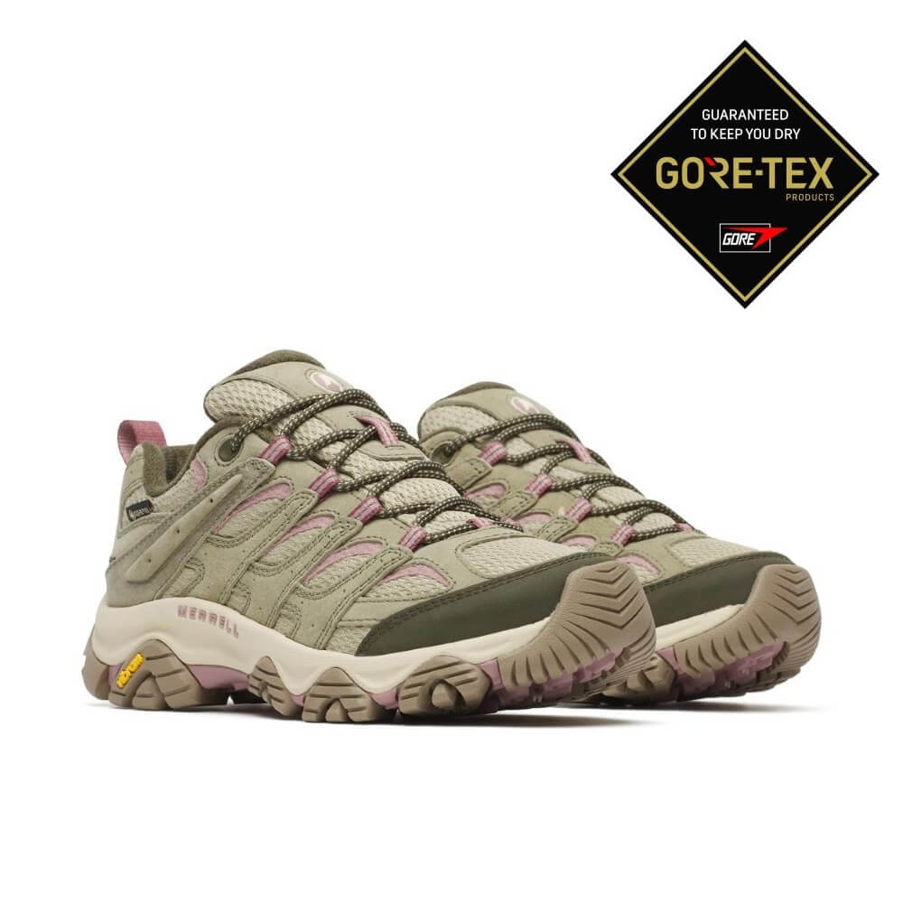 A pair of Merrell hiking shoes in olive green and beige with light pink accents, shown in profile against a white background. A  GORE-TEX guarantee badge is in the top right corner.