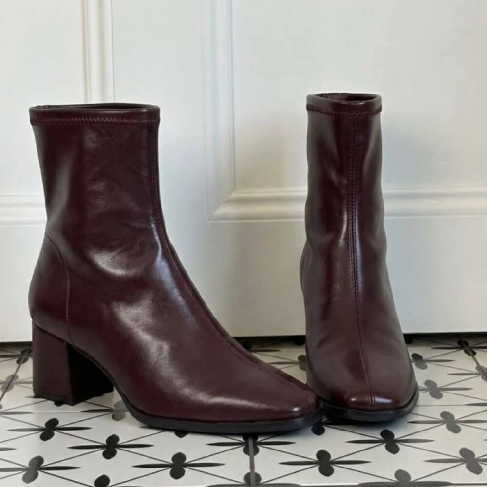 A pair of Miss Elastic dark burgundy leather ankle boots with block heels, shown from the side and back on a black and white patterned tile floor in front of a white panelled wall.
