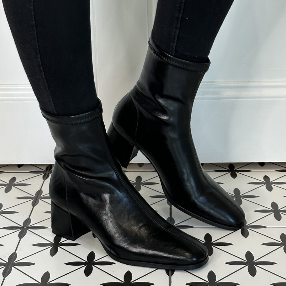Black faux leather ankle boots worn with black pants on a patterned floor. Miss Elastic 78330 Ankle Boot