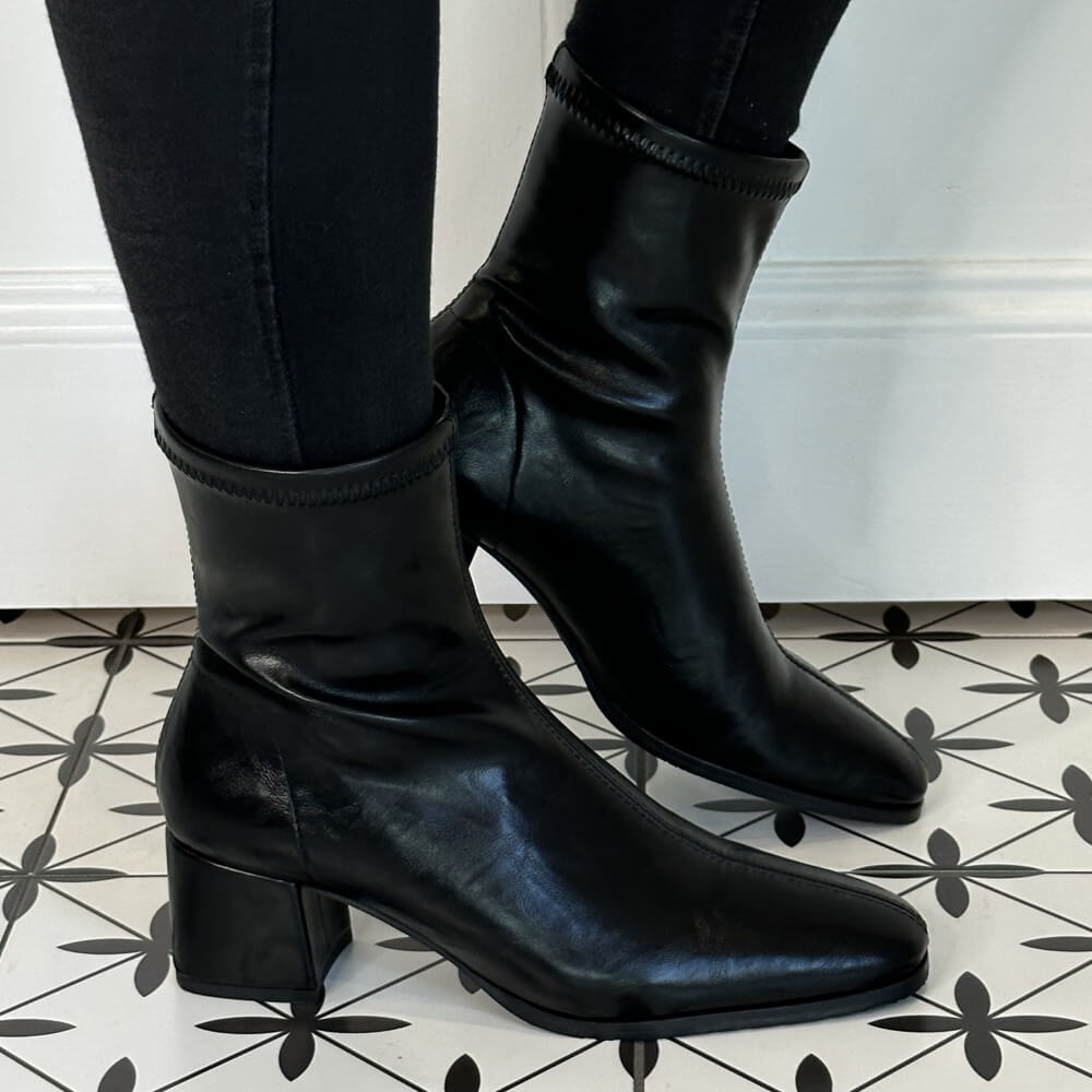 Black faux leather ankle boots worn with black pants on a patterned floor. Miss Elastic 78330 Ankle Boot