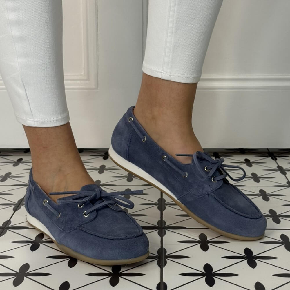 Blue suede boat shoes worn with white pants on a patterned floor.