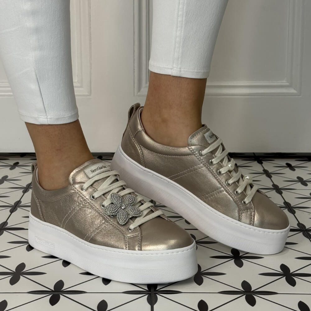 Gold sneakers with white soles worn by a person on a patterned floor. NeroGiardini E615312D