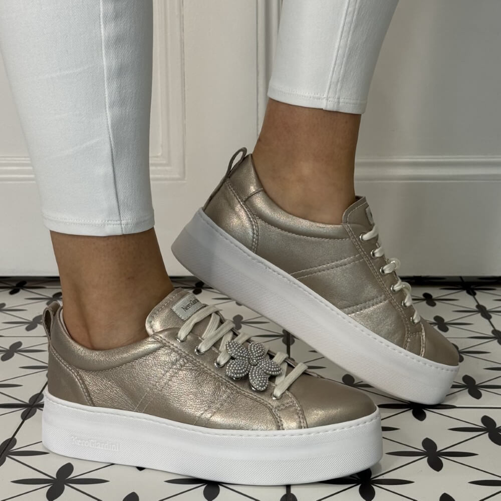 Gold sneakers with white soles worn by a person on a patterned floor. NeroGiardini E615312D